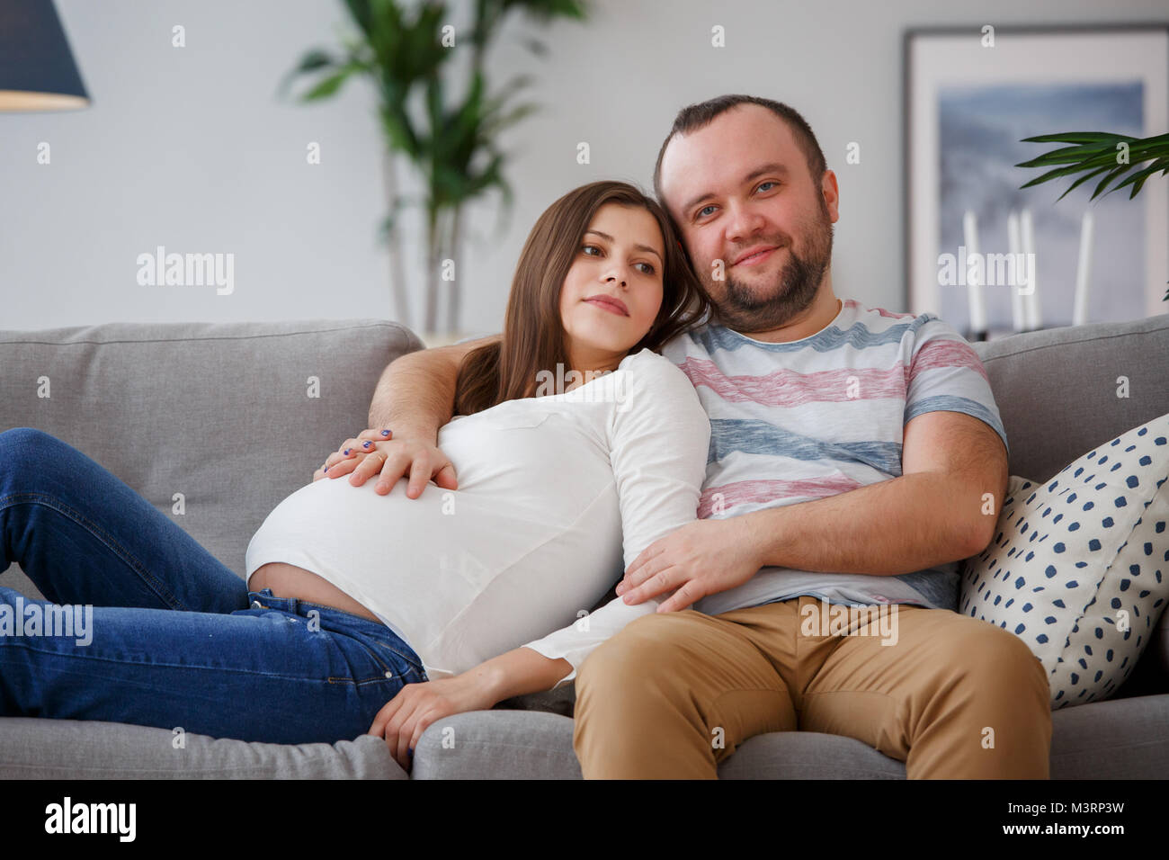 Picture of happy future parents sitting on gray sofa Stock Photo