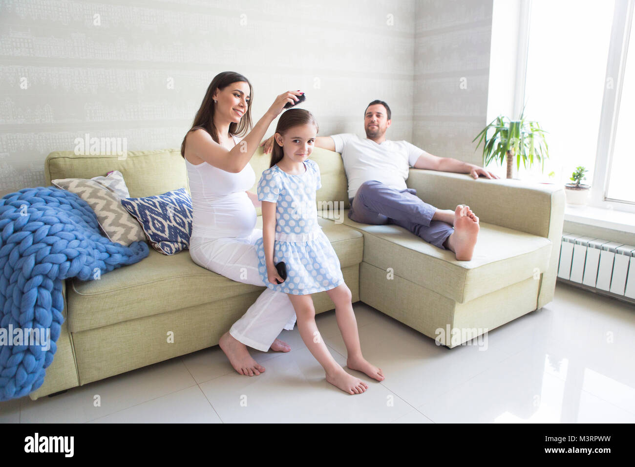 Adorable young pregnant family in living room. Mother combing her daughter's hair. Happiness and love concept Stock Photo