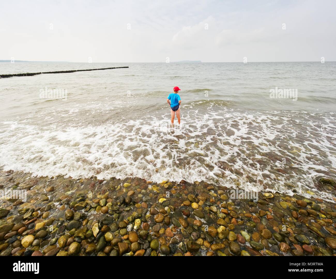 Children on the beach go into the ocean. Kid play in the waves of foamy sea. Stock Photo