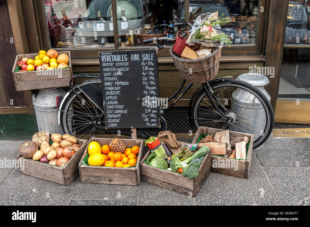 Vegetables for sale surround by an old fashioned delivery bike with baskets of fruit galvanised milk churn and advertising board outside a traditional Stock Photo