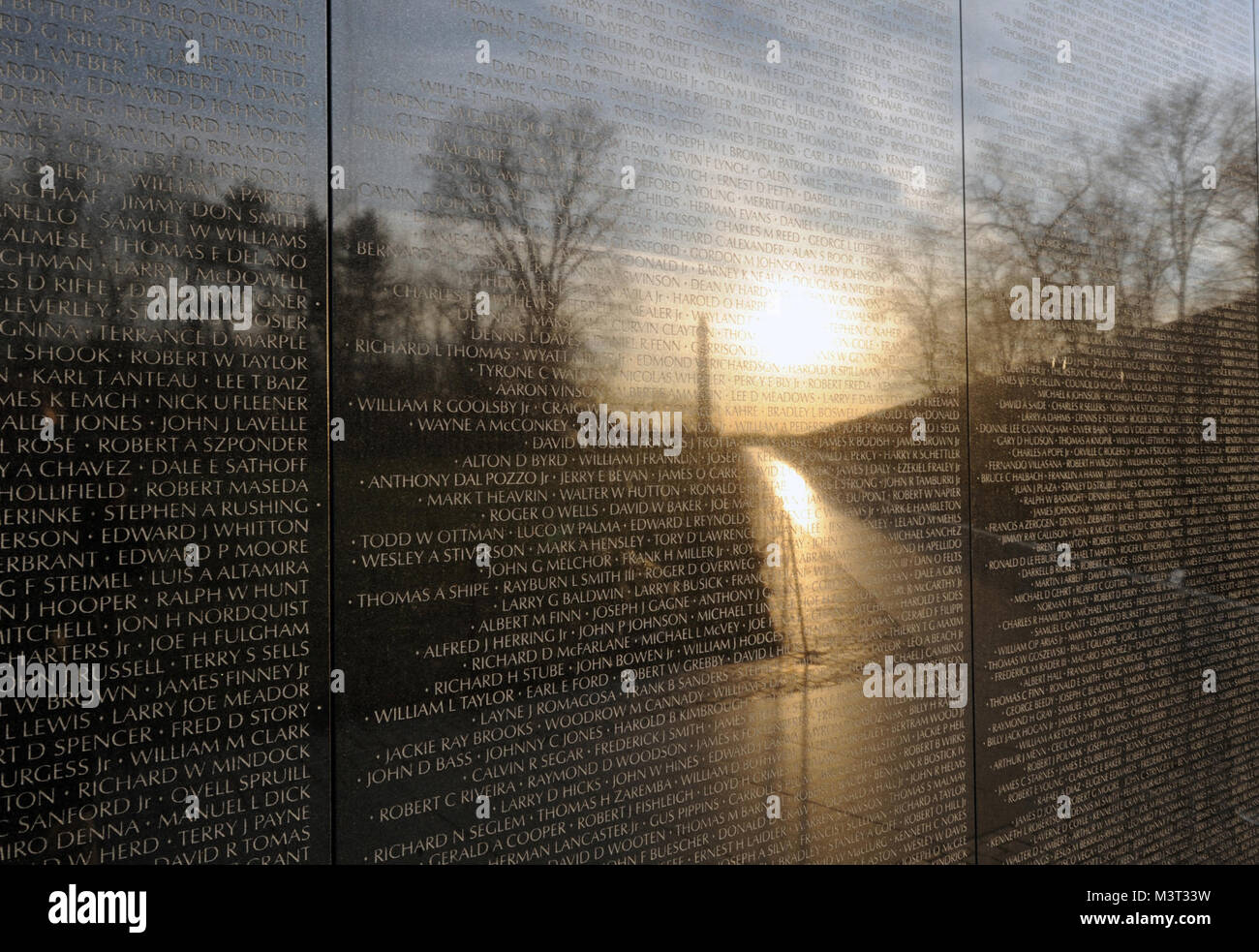 Early morning photograph of the Vietnam Memorial Wall with the reflection of the Washington Monument.  The Memorial Wall is made up of two 246 feet 9 inches (75.21 m) long gabbro walls, etched with the names of the servicemen being honored in panels of horizontal rows with regular typeface and spacing.   The walls are sunk into the ground, with the earth behind them. At the highest tip (the apex where they meet), they are 10.1 feet (3.1 m) high, and they taper to a height of 8 inches (20 cm) at their extremities. Symbolically, this is described as a 'wound that is closed and healing.'  (Depart Stock Photo