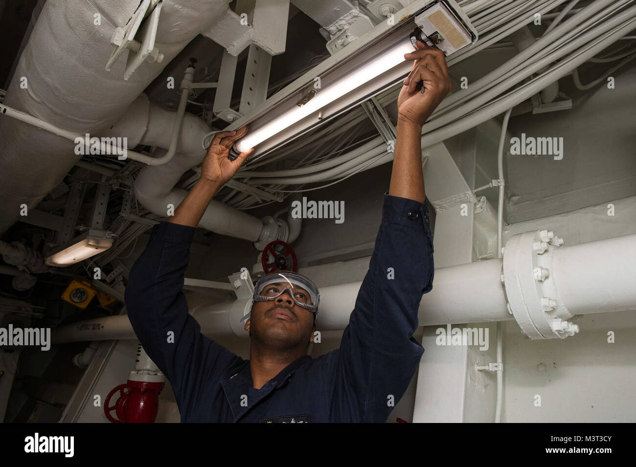160406-N-MD297-004 PACIFIC OCEAN (April 6, 2016) - Operations Specialist 2nd Class Christopher Thomas replaces a fluorescent light bulb with a more energy efficient LED light bulb in a passageway aboard the Arleigh Burke-class guided-missile destroyer USS Lassen (DDG 82). Lassen is currently underway in support of Operation Martillo, a joint operation with the U.S. Coast Guard and partner nations within the 4th Fleet area of responsibility. Operation Martillo is being led by Joint Interagency Task Force South, in support of U.S. Southern Command. (U.S. Navy photo by Mass Communication Speciali Stock Photo