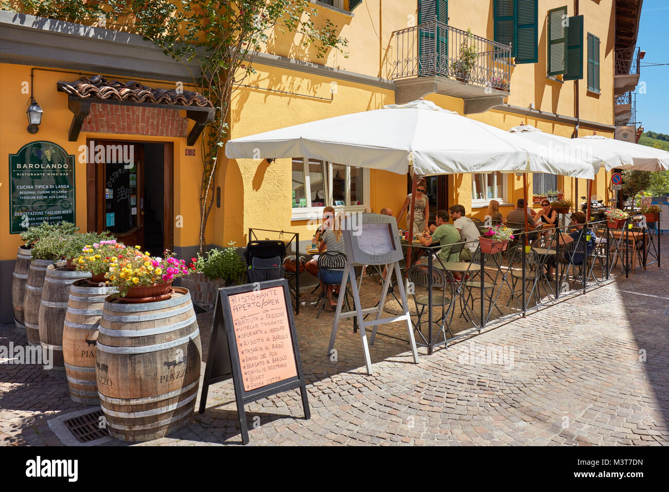 Sidewalk typical restaurant with people in a sunny summer day in Piedmont in Barolo, Italy. Stock Photo