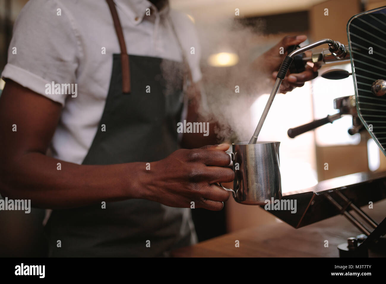 Coffee shop owner preparing coffee on steam espresso coffee machine. Cropped shot of man working in his coffee shop wearing an apron. Stock Photo