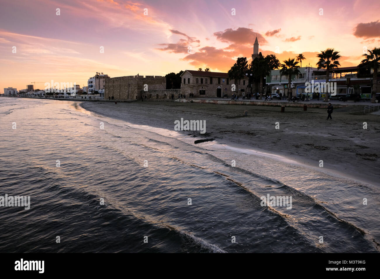 Larnaca, CYPRUS - January 2 2018: People by the waterfront in the city center of Larnaca in sunset light. View towards Larnaca castle and Kebir-Buyuk  Stock Photo