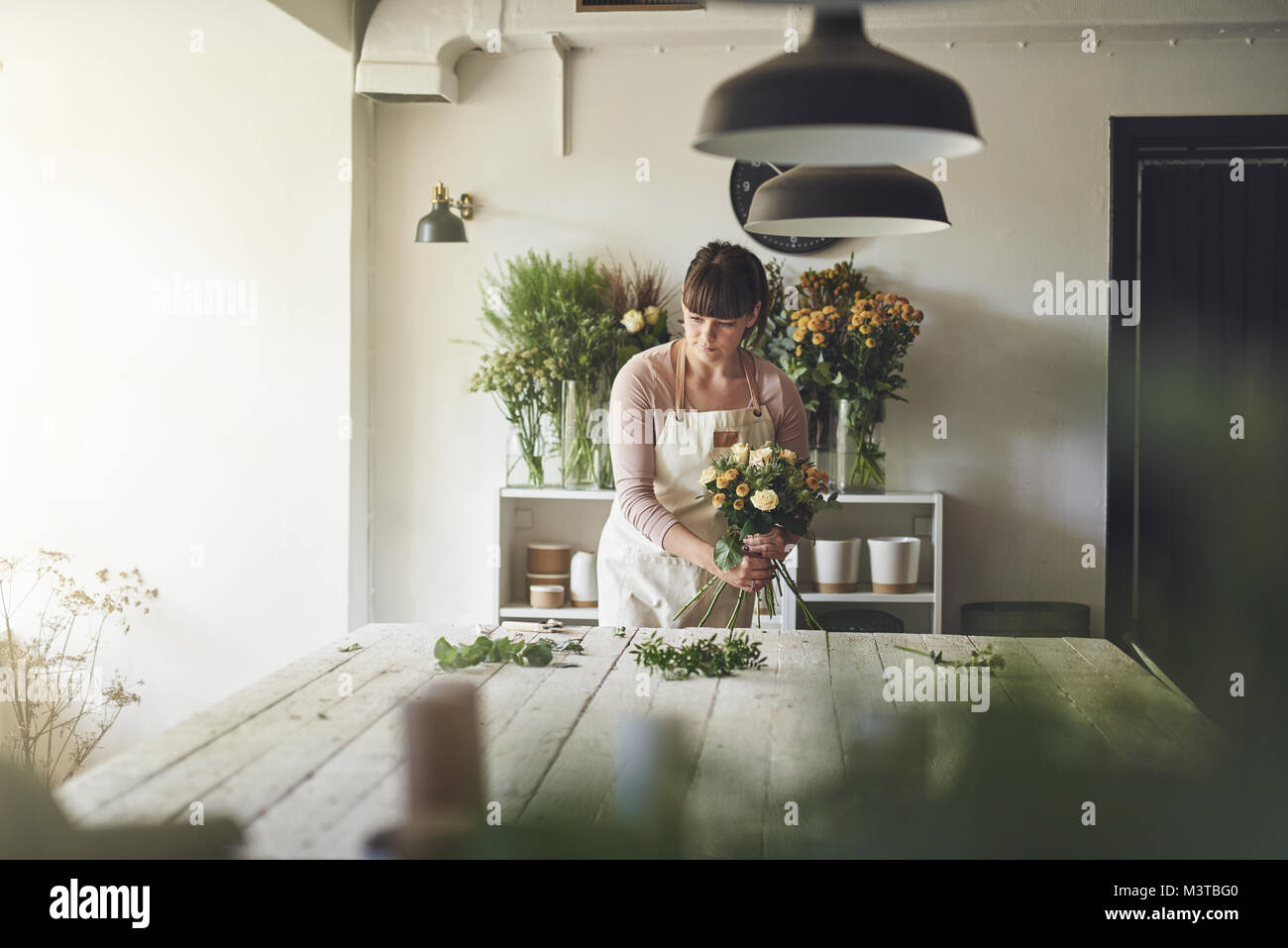 Young female florist working at a table in her flower workshop arranging a bouquet of mixed flowers Stock Photo
