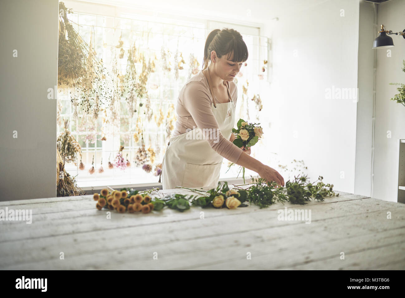 Young female florist arranging a bouquet of mixed flowers while standing at a table in her flower workshop Stock Photo