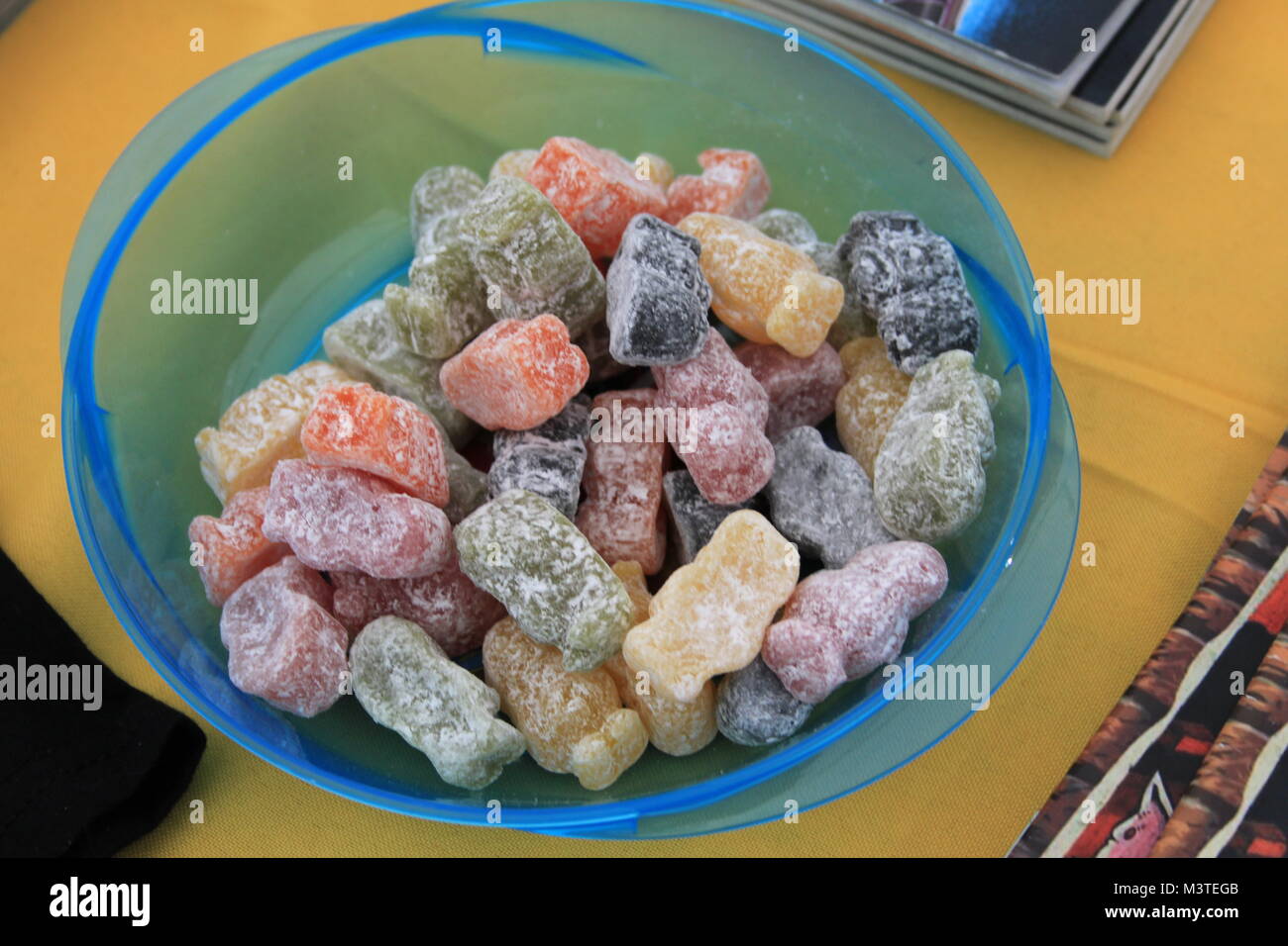 Blue plastic bowl filled with colourful jelly baby sweets on a light coloured wooden table. Jelly babies are traditional British jelly sweets. Stock Photo