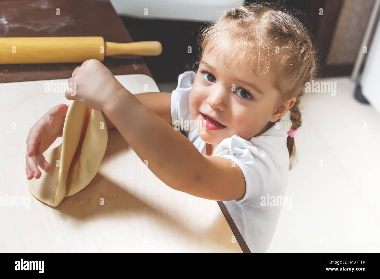 Little pretty girl is cooking dough in the kitchen at home to help her