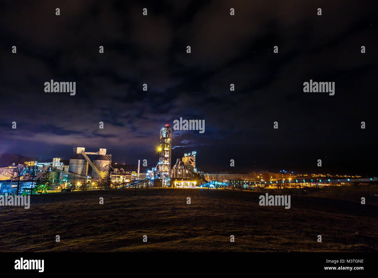 Industrial facility with lights at night under starry sky with clouds