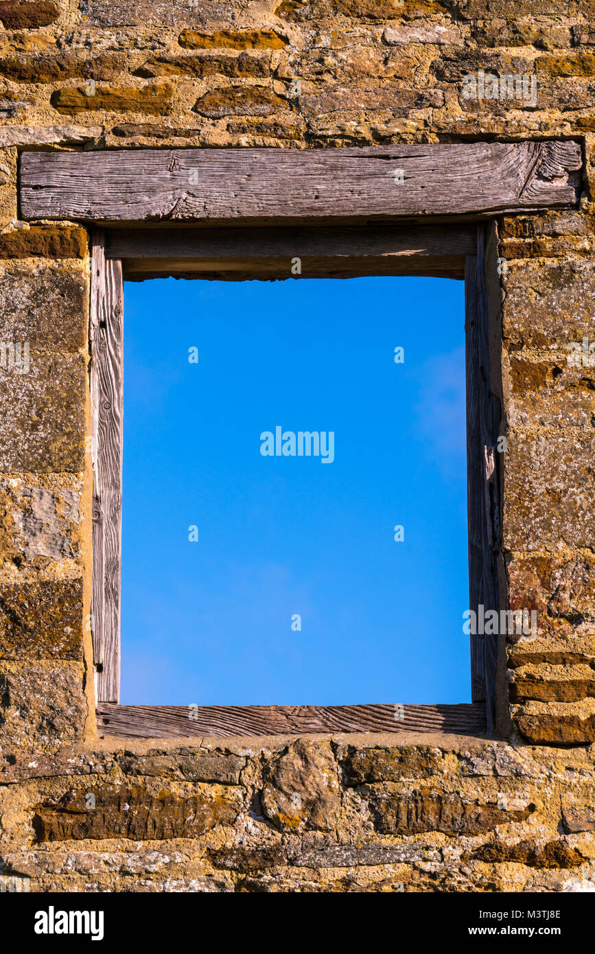 Window frame in an old stone wall onto a blue sky. No glass and a wooden frame and lintel Stock Photo