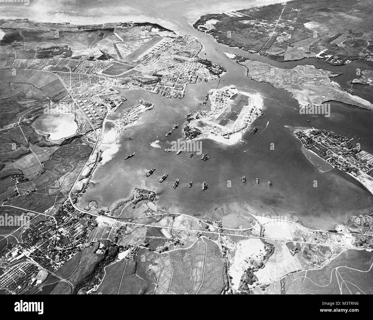 Aerial view of the U.S. Naval Operating Base, Pearl Harbor, Oahu, Hawaii (USA), looking southwest on 30 October 1941. Ford Island Naval Air Station is in the center, with the Pearl Harbor Navy Yard just beyond it, across the channel. The airfield in the upper left-center is the U.S. Army's Hickam Field. Pearl Harbor looking southwest-Oct41 by AirmanMagazine Stock Photo