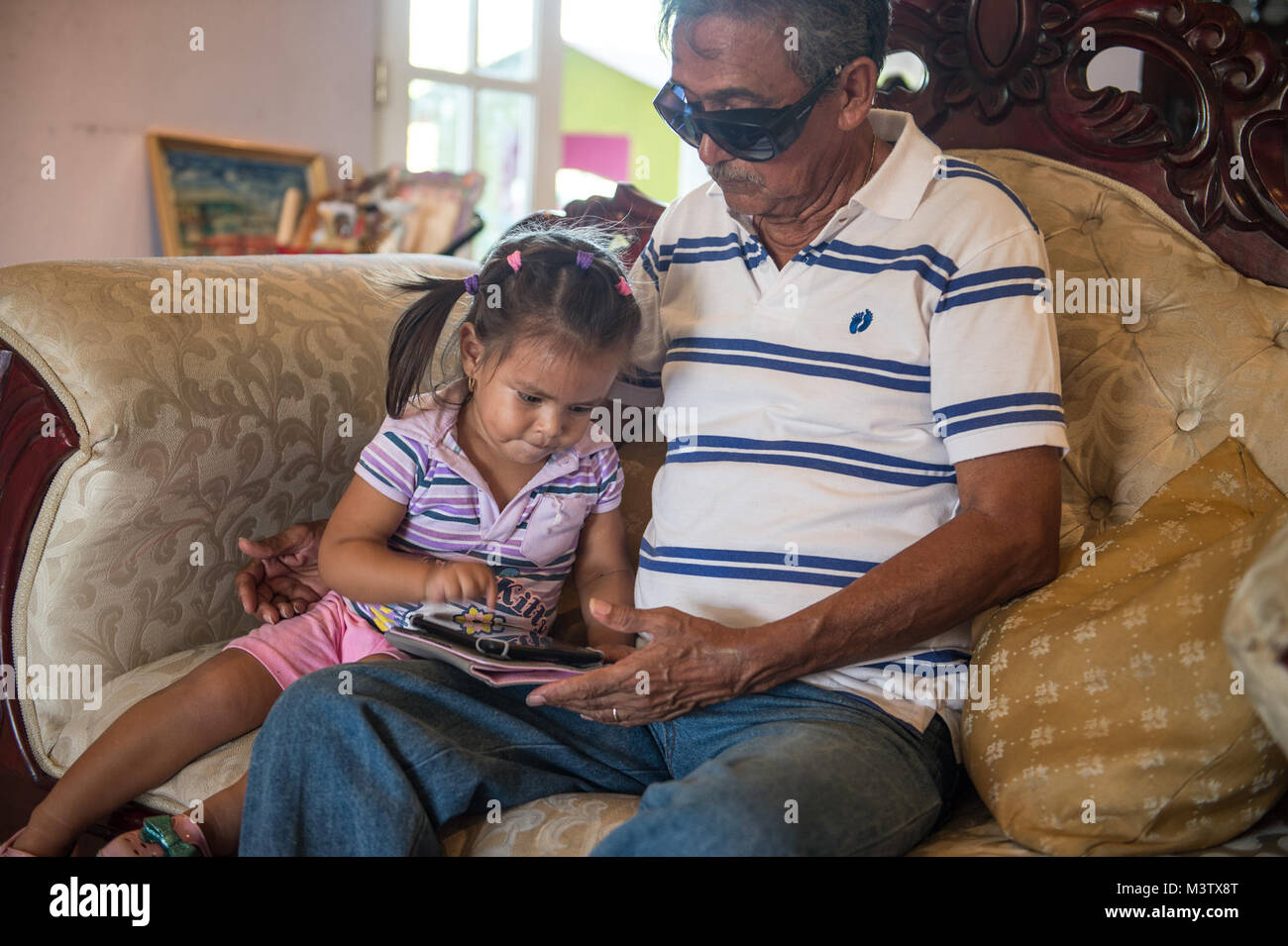 Eduardo Barrera looks at a tablet with his grandchild, Feb. 7, 2017, after having an extracapsular cataract extraction with intraocular implant surgery the day before at the Centro Hospitalario Luis 'Chicho' Fabrega during a medical readiness training exercise in Santiago, Panama. A U.S. military medical team was in Panama to help treat individuals with cataracts that otherwise would have gone untreated. Medical readiness training exercises provide U.S. military personnel training in delivery of medical care in austere conditions, promote diplomatic relations between the U.S. and host nations  Stock Photo