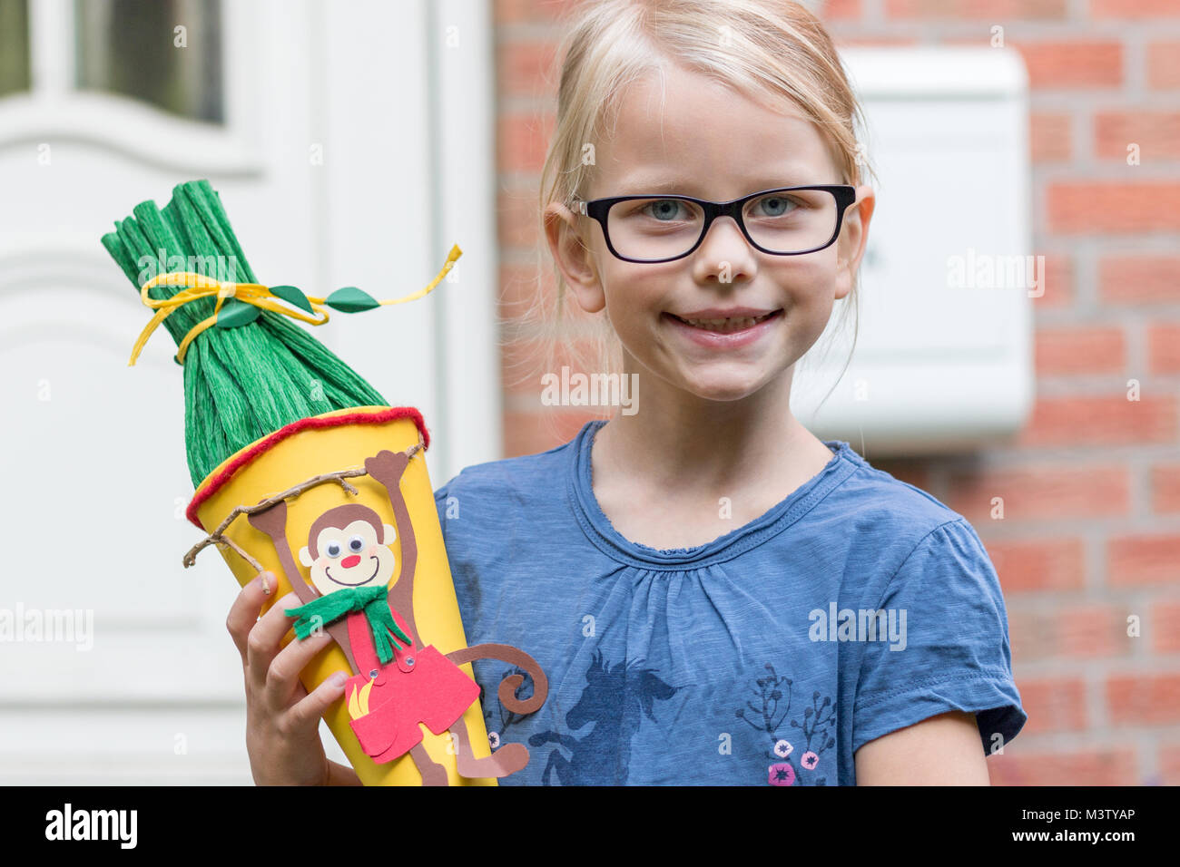 A blond girl in glasses looks forward to his first day at school and poses with the school bag on her doorstep. Stock Photo