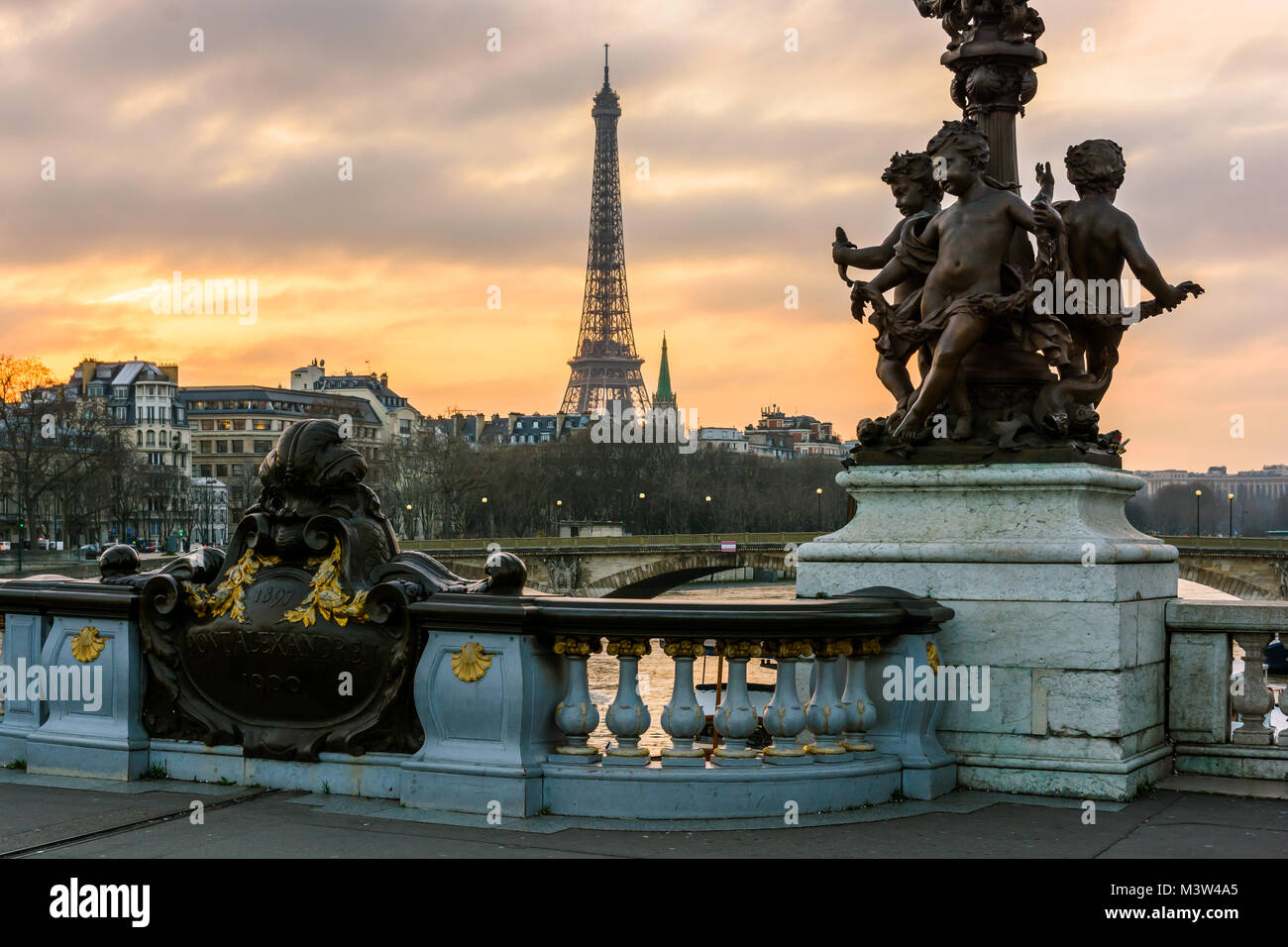 View of the Eiffel tower from the Pont Alexandre III at sunset with the cherubs ornamenting one of its Art Nouveau street lamp in the foreground. Stock Photo