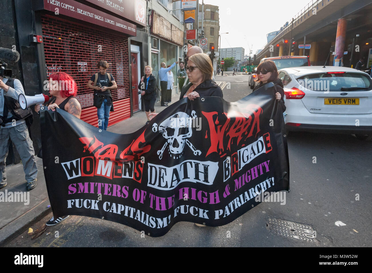 After a short protest on the opposite side of the road, protesters cross the road with the Class War Womens Death Brigade banner to protest outside the Jack the Ripper museum Stock Photo