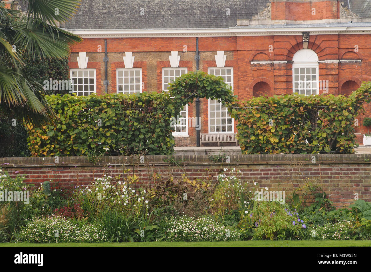 A view of part of Kensington Palace from the sunken garden with the garden wall and a trained hedge archway Stock Photo