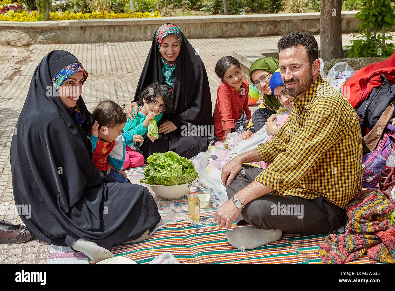 Tehran, Iran - April 28, 2017: Iranian man, children and women in hijabs sit in the park on a picnic on the day off, they smile and laugh. Stock Photo