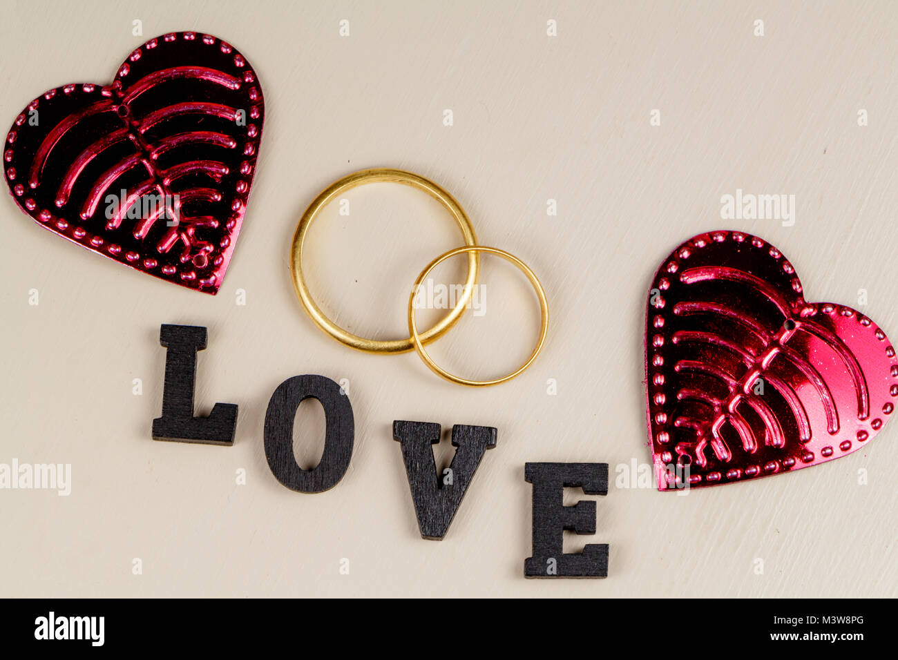 Two wedding rings in gold, two pink hearts and the word love in black letters Stock Photo