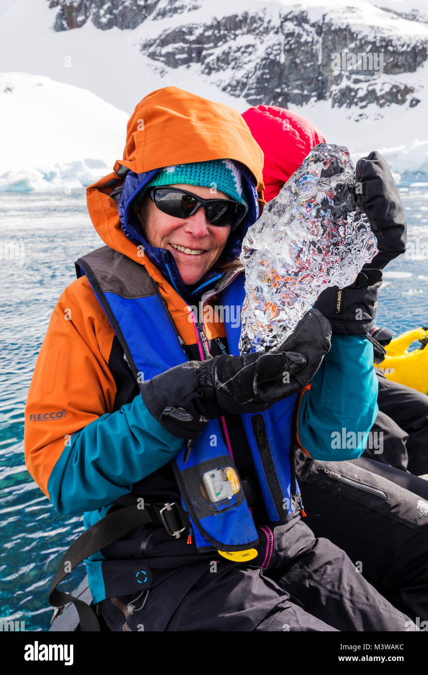 Expedition member in Zodiac boat holds crystal clear glacial ice; Zodiacs shuttle alpine mountaineering skiers to Antarctica from the passenger ship O Stock Photo