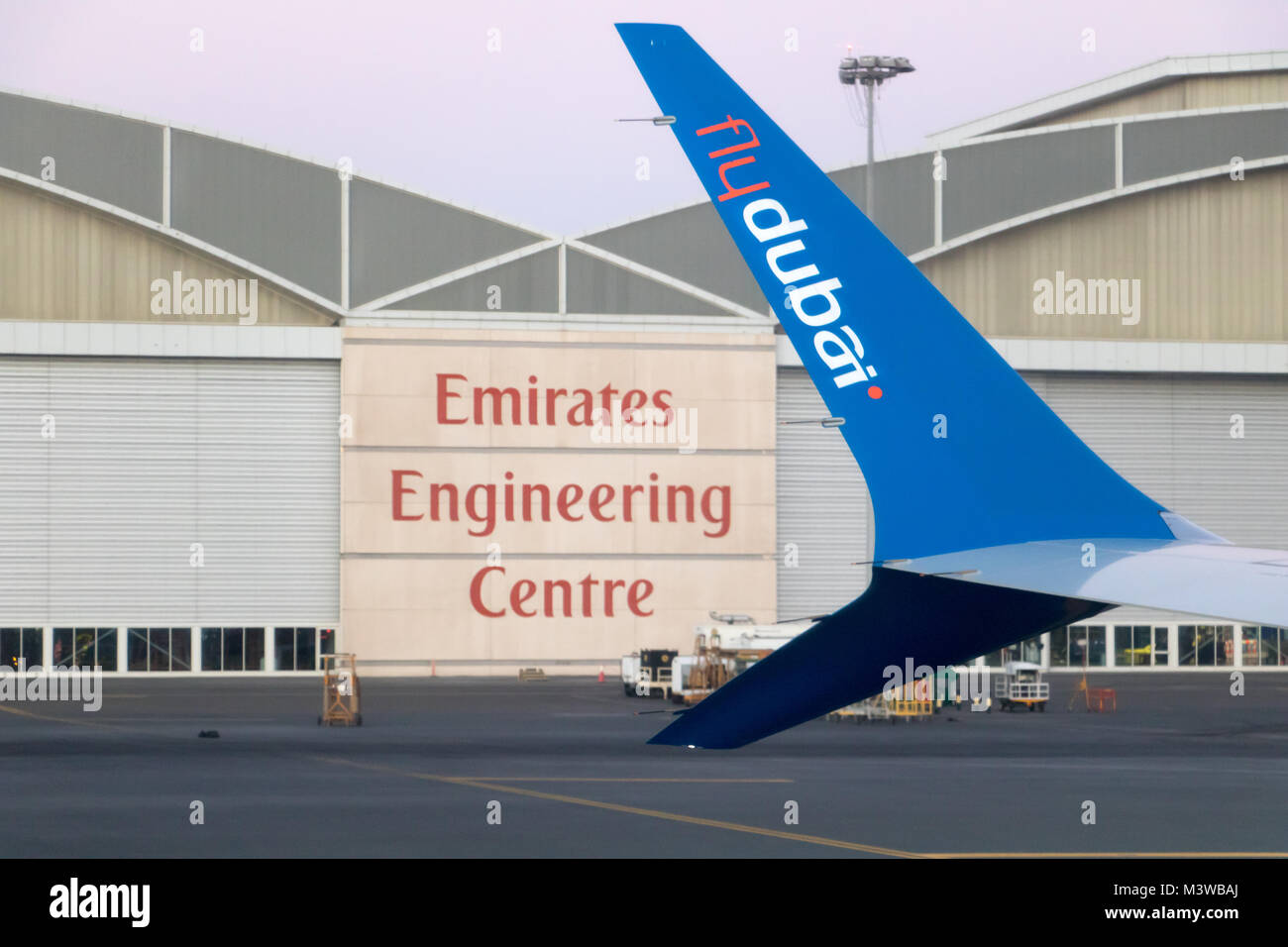 The airplane of Flydubai aircraft company standing at ramp, hangar of Emirates aircraft company at background. Stock Photo