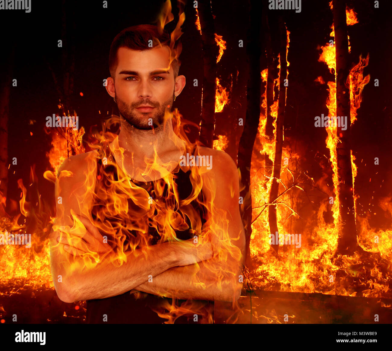 Young man stands with arms crossed as flames burn over his torso Stock Photo