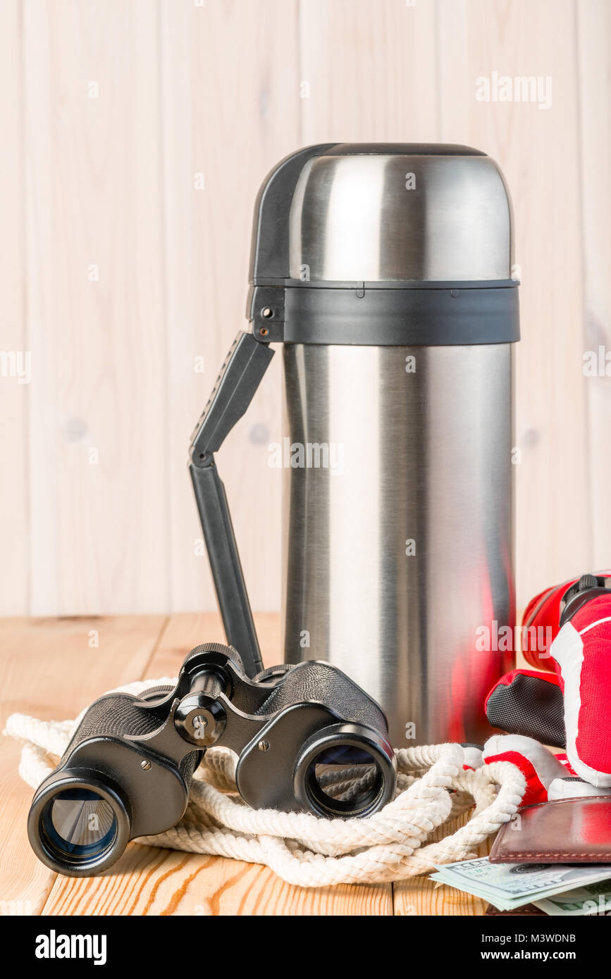 thermos with hot tea, binoculars, rope and gloves for a dangerous winter hike on a wooden background Stock Photo