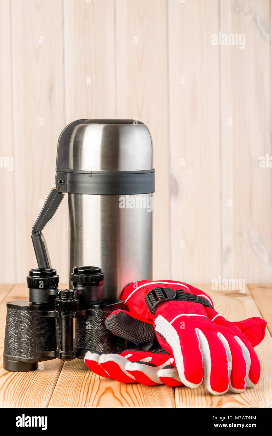 binoculars, gloves and thermos with tea ready for a difficult hike, objects on a wooden background Stock Photo