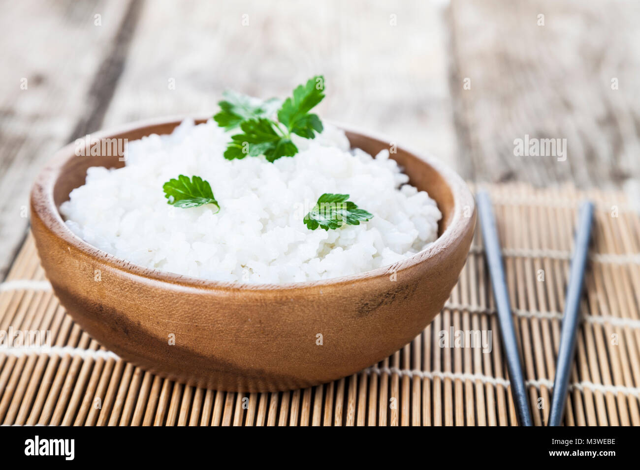 Boiled rice in a wooden bowl and chopsticks on the table. Delicious vegetarian dinner. Stock Photo