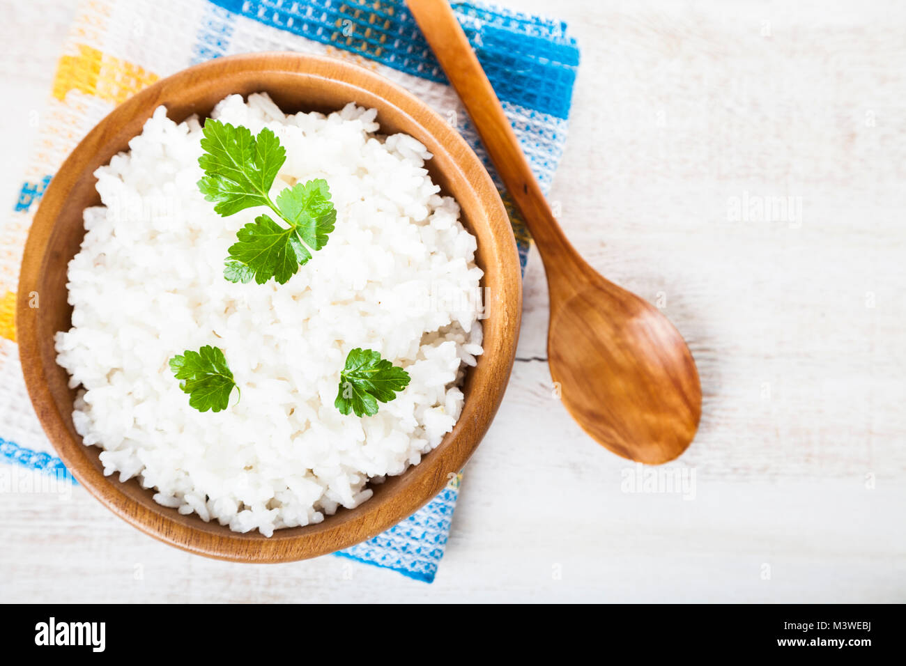 Boiled rice in a wooden bowl and spoon on the table. Delicious vegetarian dinner. Stock Photo