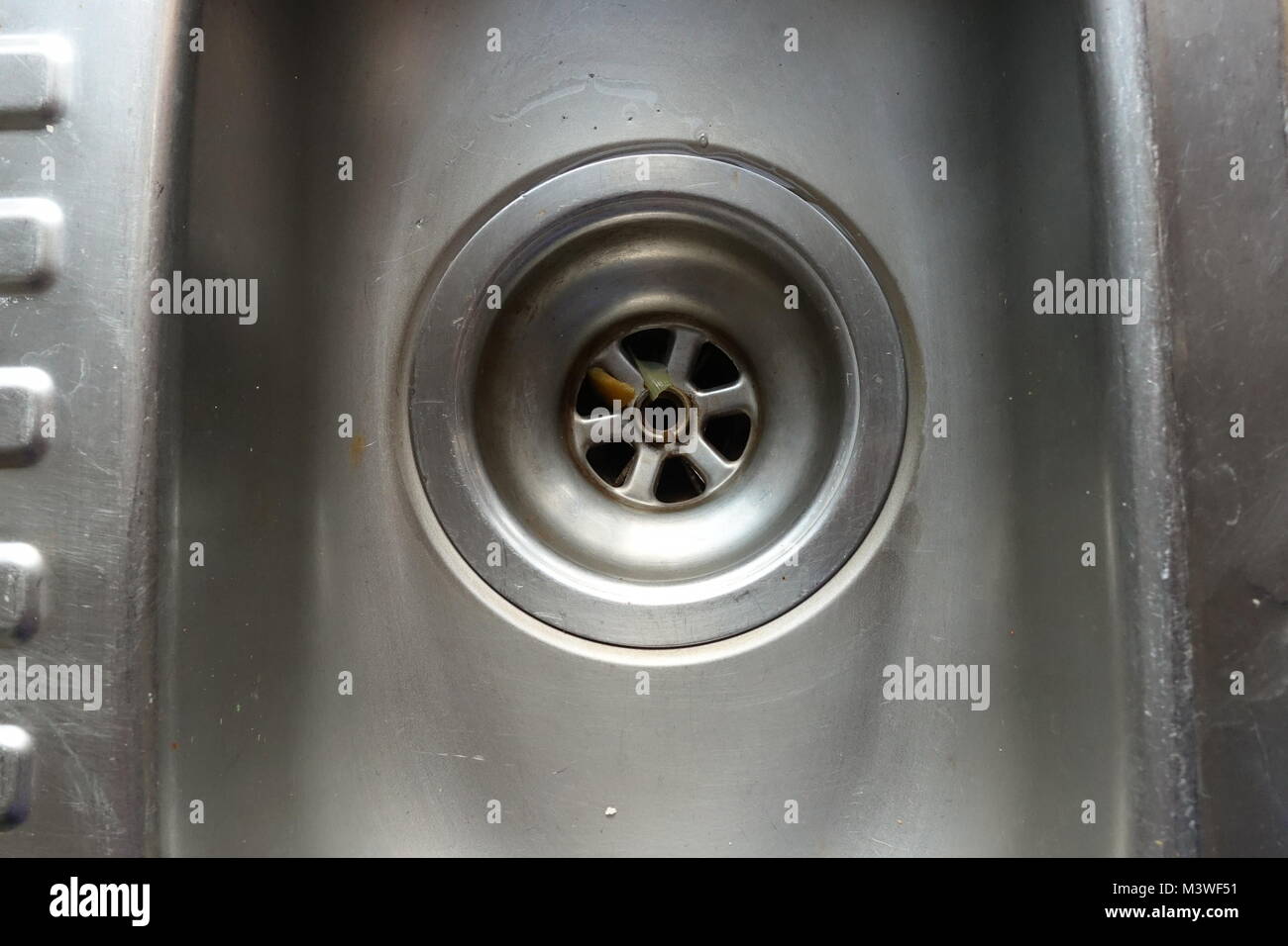 Dirty and scratched domestic kitchen sink and plug hole with scraps of