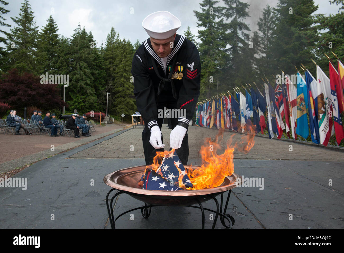 BANGOR, Wash. (June 14, 2017) Electronics Technician (Communications) 1st Class Jonathan Diquattro, from Columbus, Georgia, assigned to Trident Training Facility Bangor, places the remains of a U.S. flag to a fire during a flag retirement ceremony at Naval Base Kitsap - Bangor. When a U.S. flag becomes worn, torn, faded, or badly soiled, the flag should be retired with the dignity and respect befitting it. The traditional method is to cut the flag into pieces, separating the 13 stripes from canton and incinerating them separately in a respectful manner. (U.S. Navy photo by Mass Communication S Stock Photo