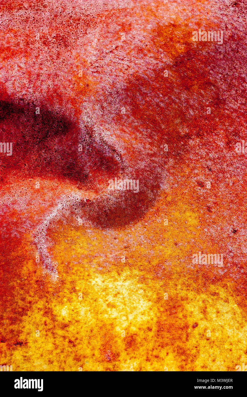 Vivid red and yellow colors produced by the oxidization, rusting, of a dented, metal sheet. Stock Photo