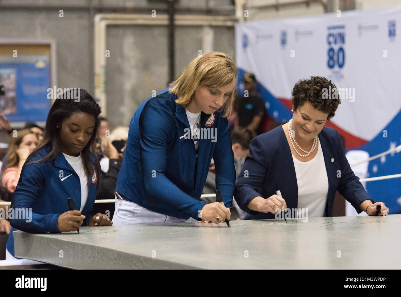 170824-N-N0101-110 NEWPORT NEWS, Va. (Aug. 24, 2017) U.S. Olympic gold medalists Simone Biles, left, and Katie Ledecky, ship’s sponsors of the future aircraft carrier USS Enterprise (CVN 80), and Jennifer Boykin, president of Newport News Shipbuilding, sign a 35-ton steel plate at Newport News Shipbuilding to start advance construction of Enterprise, the ninth U.S. Navy ship to bear the name. Enterprise will be the third Gerald R. Ford-class aircraft carrier. (U.S. Navy photo courtesy of Huntington Ingalls Industries by Matt Hildreth/Released) CVN80 First Cut of Steel by Photograph Curator Stock Photo