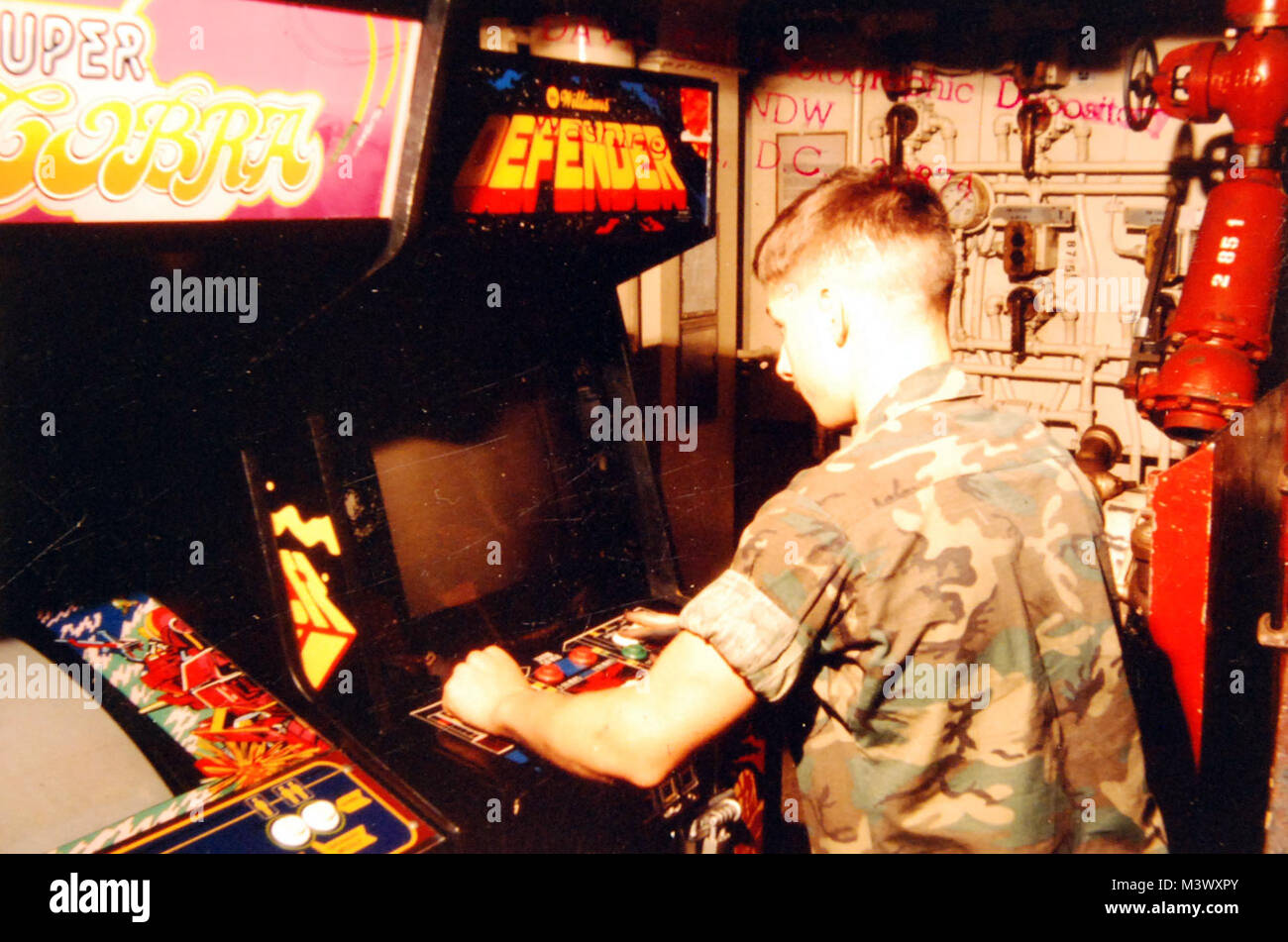 428-GX-DN-ST-84-05474:   Mediterranean Sea.  A U.S. Marine spends some of his spare time playing a video game in the game room on the aircraft carrier USS America (CV-66).   Photographed by Defosse, August 23, 1982.  Official U.S. Navy Photograph, now in the collections of the National Archives.  (2017/12/13).  Photographed from a small reference card. 428-GX-DN-ST-84-05474 25166529858 o Stock Photo