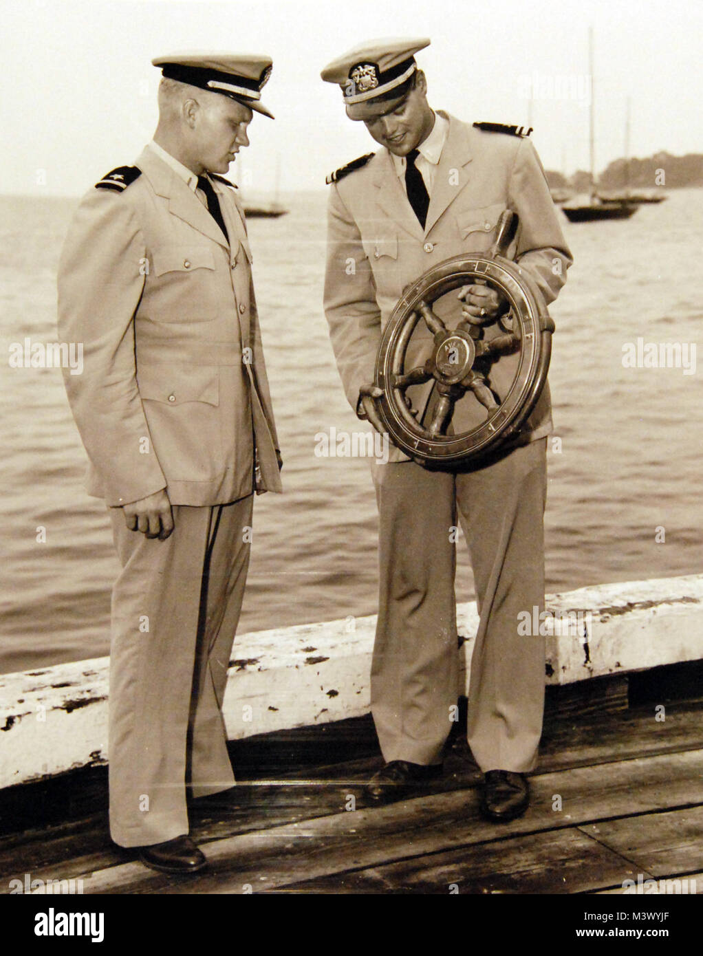 80-G-680535:  Wheel from the auxiliary yawl, Avanti, which was destroyed during Hurricane Carol in 1954, has been presented to the Naval Academy, Annapolis, Maryland, as a permanent sailing trophy by Mr. Walter Rothschild of Brooklyn, New York.   Looking over the newest sailing trophy are Ensign G.T. Akins, left, and Lieutenant Junior Grade J. M. McDonald.  Official U.S. Navy Photograph, now in the collections of the National Archives.  (2018/01/17). 80-G-680535 38850490185 o Stock Photo