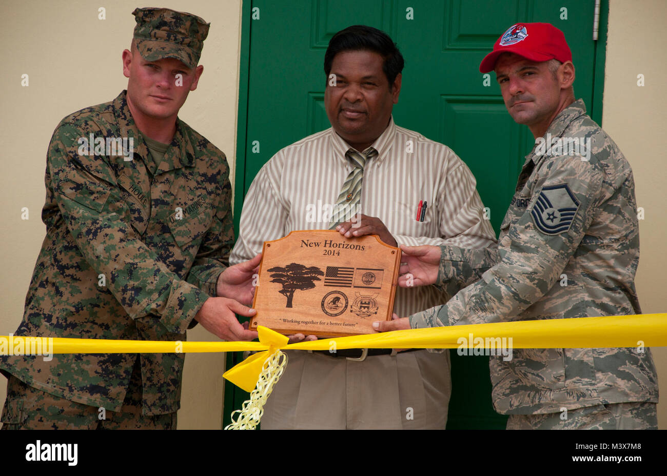 U.S. Marine Corps Staff Sgt. Matt Houle, construction site foreman, left, and U.S. Air Force Master Sgt. Nicholas Alessi, construction site project manager, right, present a plaque to Rodrick Cardinez, Edward P. Yorke school principal, during the ribbon cutting ceremony June 4, 2014, at the school in Belize City, Belize. The school's 1,372 square foot, two-classroom addition is one of five New Horizons projects in the country. New Horizons is an annual multinational exercise that provides training opportunities in civil engineering and medical care. (U.S. Air Force photo by Tech. Sgt. Kali L.  Stock Photo