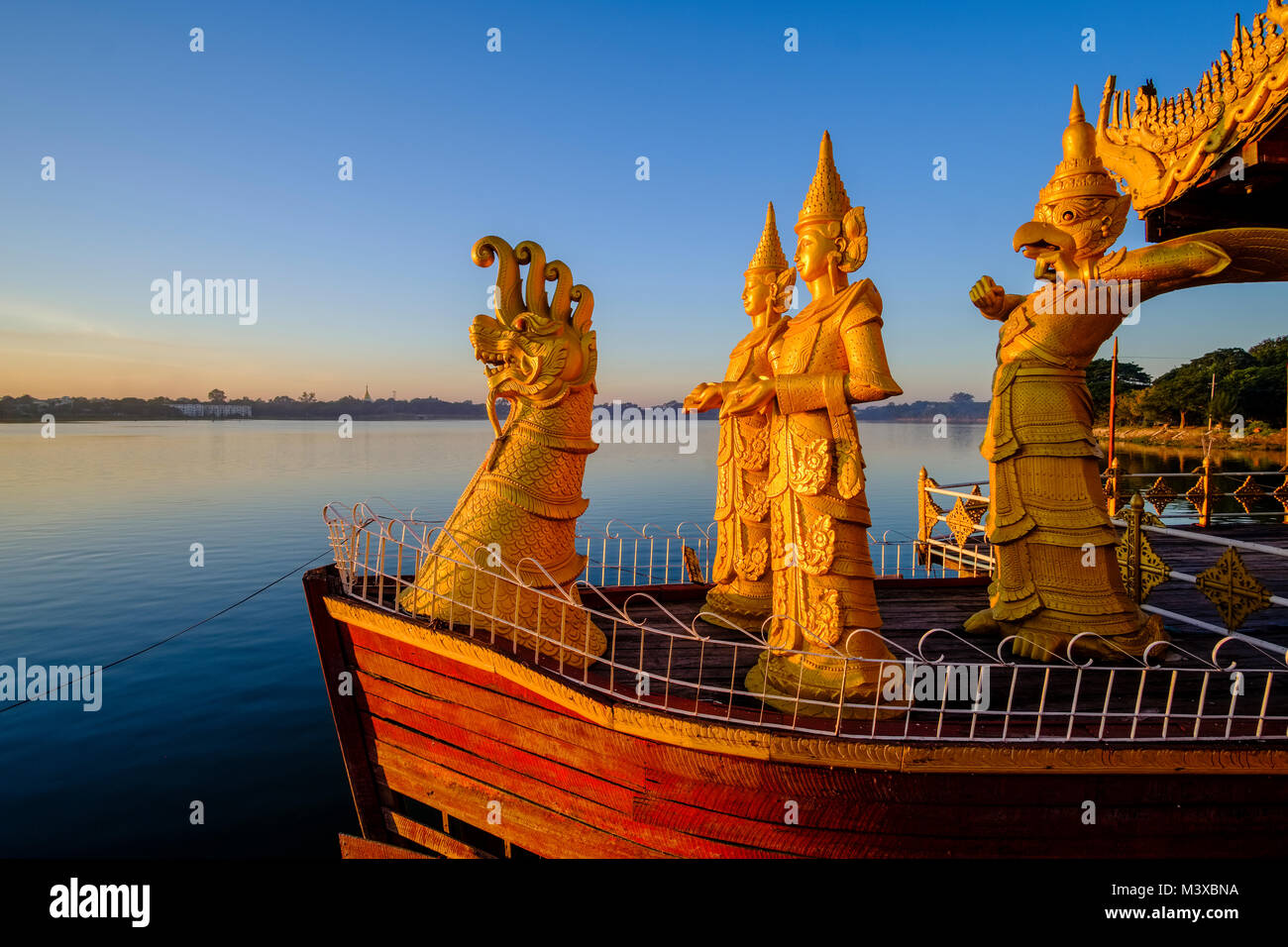 Golden statues are decorating the Pyi Gyi Mon Royal Barge, a swimming restaurant, floating on Kandawgyi Lake at sunrise Stock Photo