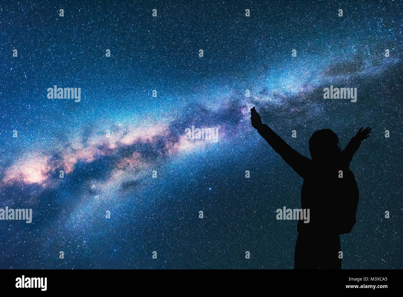Milky Way with silhouette of a happy woman with backpack and raised up arms at night. Space background with sky with stars, bright colorful milky way, Stock Photo