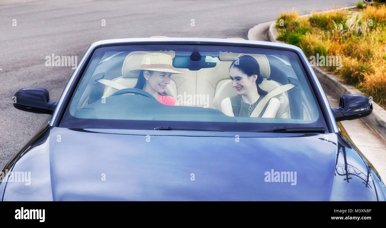 Young ladies driving a modern luxury convertible car with soft top down on a sunny summer day full of joy and happiness - seen through windscreen. Stock Photo