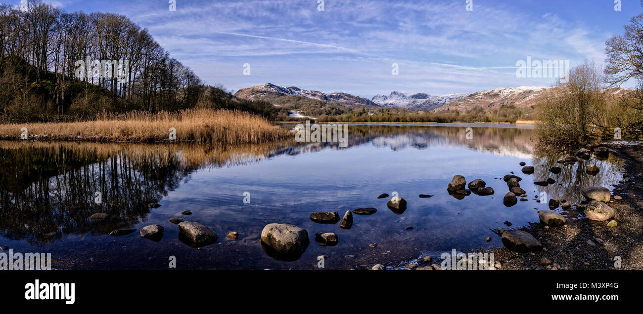 Panoramic view of Elter Water with the snow-covered Langdale Pikes behind Stock Photo