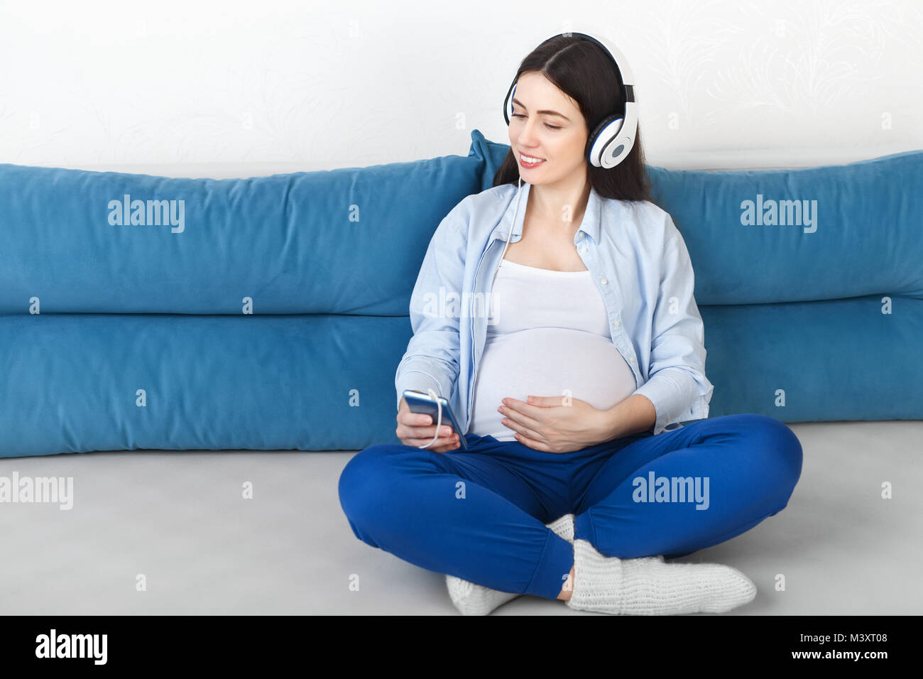 happy pregnant woman listening music in headphones and touching her belly. Pregnancy, people, technology concept Stock Photo