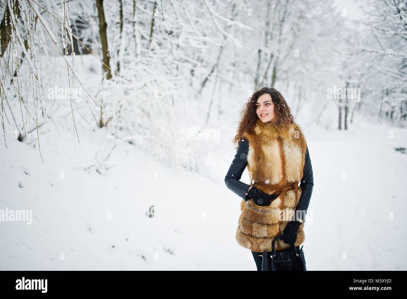 Elegance curly girl in fur coat and handbag at snowy forest park at ...