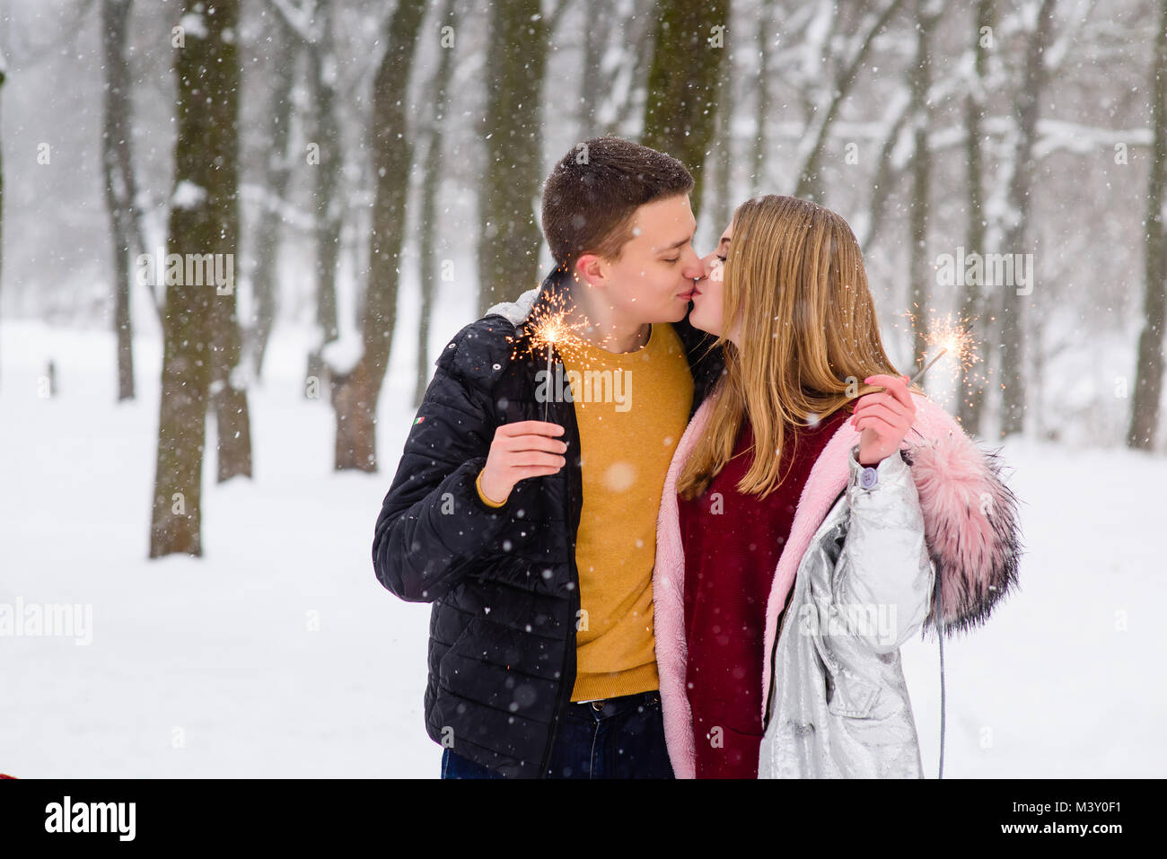Romantic kiss during snowfall in winter forest. Young couple with bengals outdoors. Stock Photo