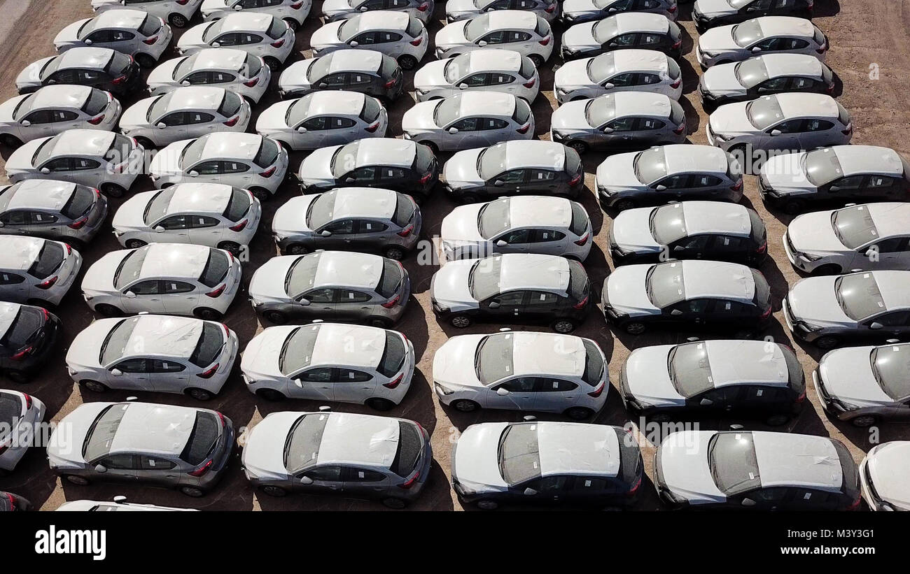 New cars covered in protective white sheets parked in a holding