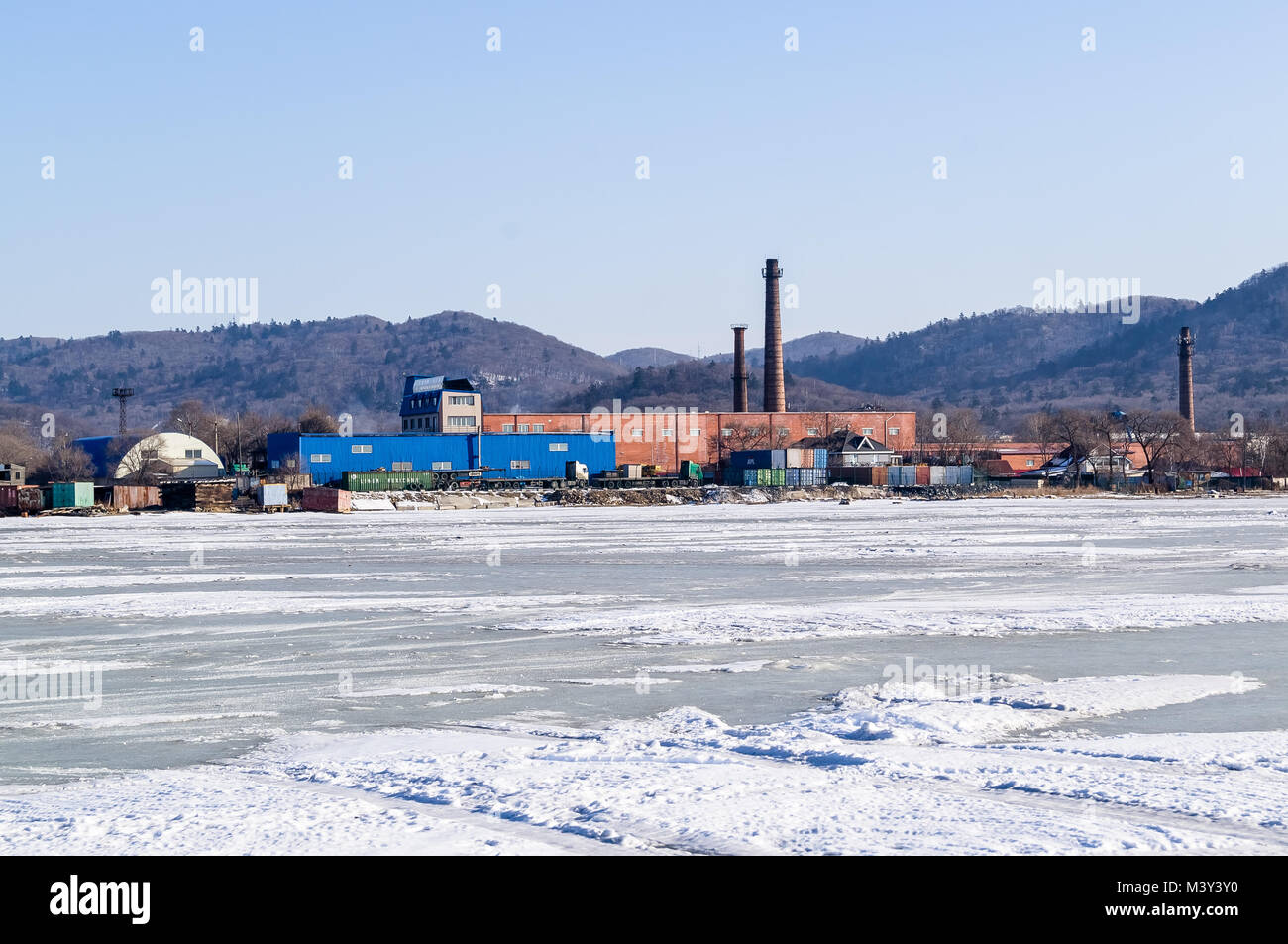 Industrial area. Production buildings. Pipes. View from the frozen sea in winter. On ice. Stock Photo