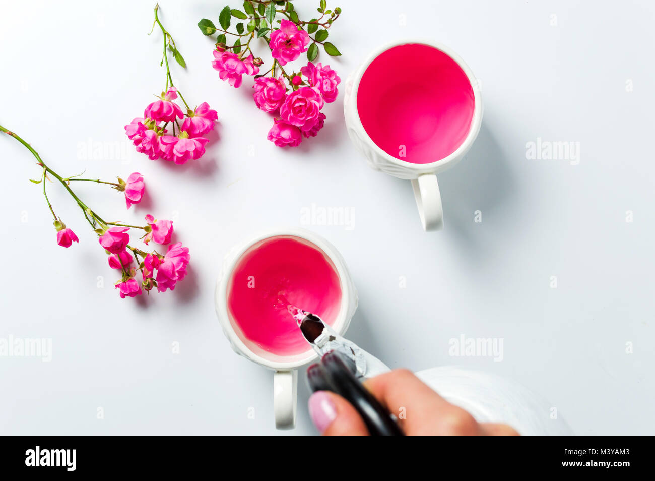 Person pouring tea with rose flowers on white table Stock Photo