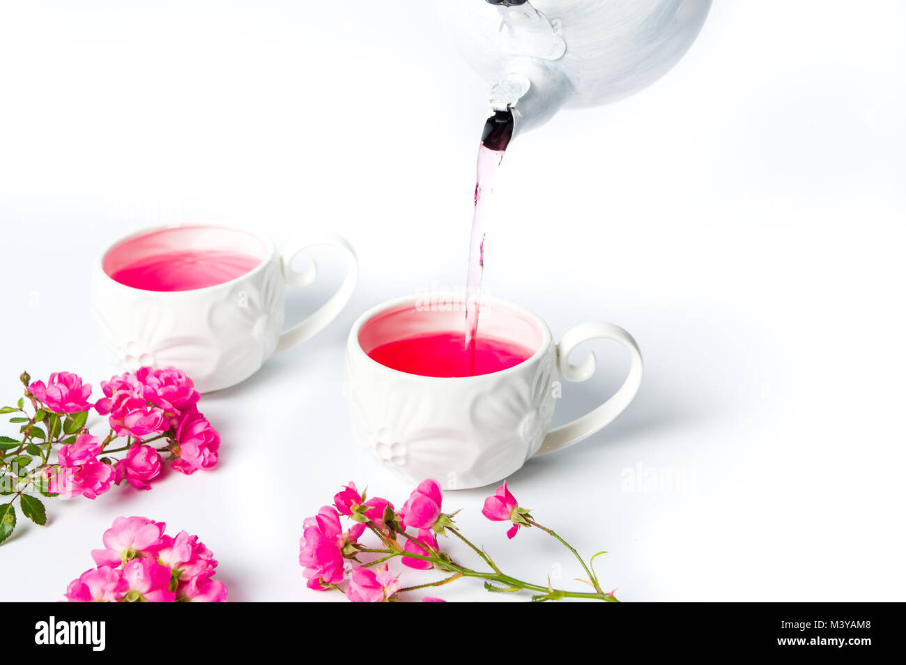 Person pouring tea with rose flowers on white table Stock Photo