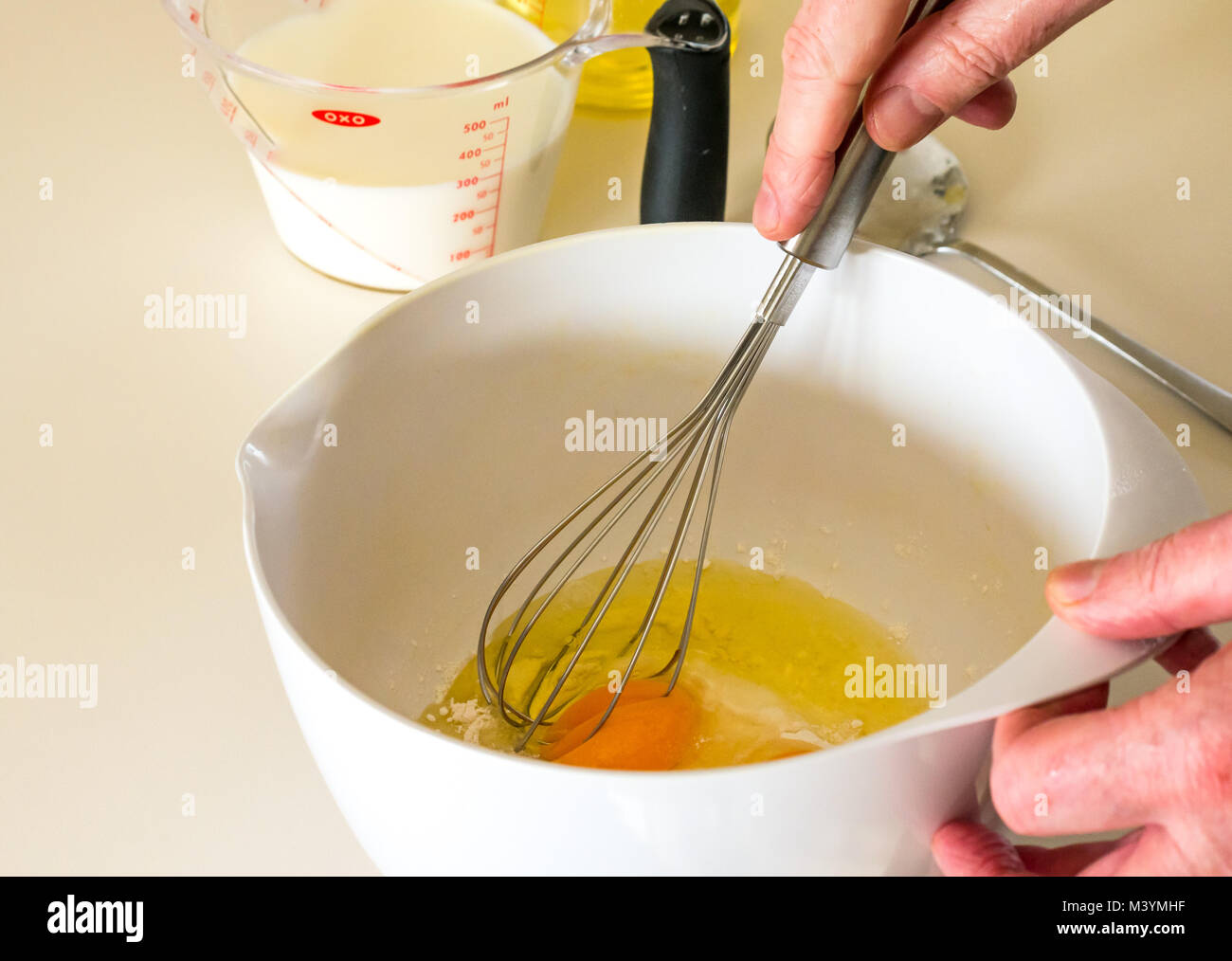 Man beating mixture with whisk to make pancake batter for Shrove Tuesday with flour, milk, eggs, and oil in a home kitchen Stock Photo