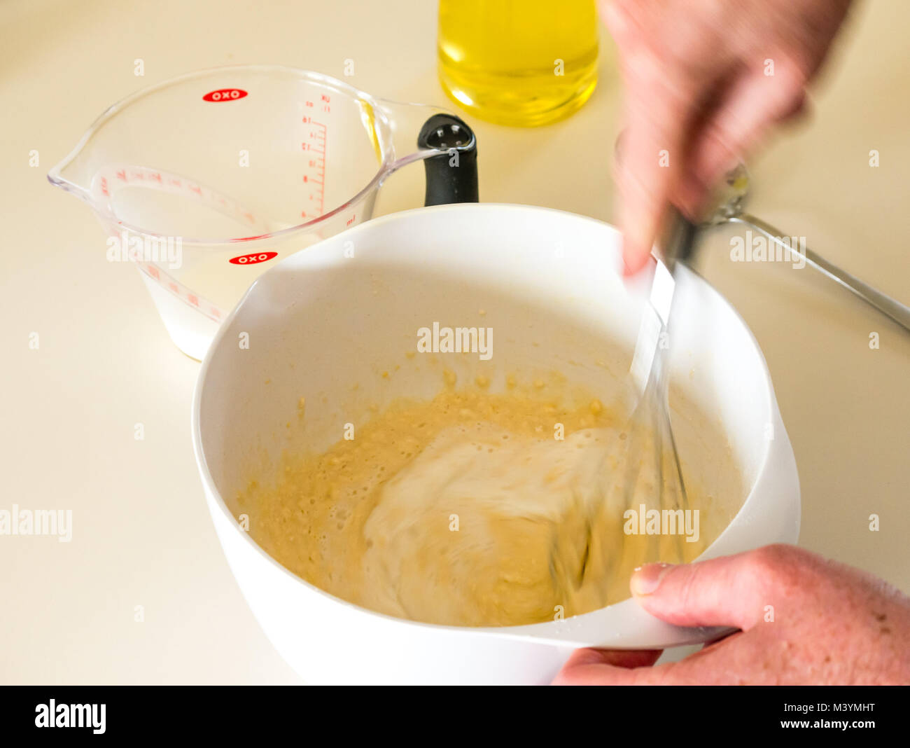 Man beating mixture with whisk to make pancake batter forShrove Tuesday with flour, milk, eggs, and oil in a home kitchen Stock Photo